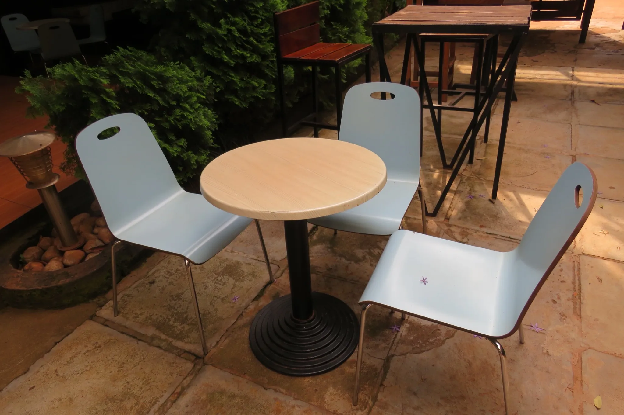 An outdoor café patio with bar-height tables and stools set among low chairs and green hedges