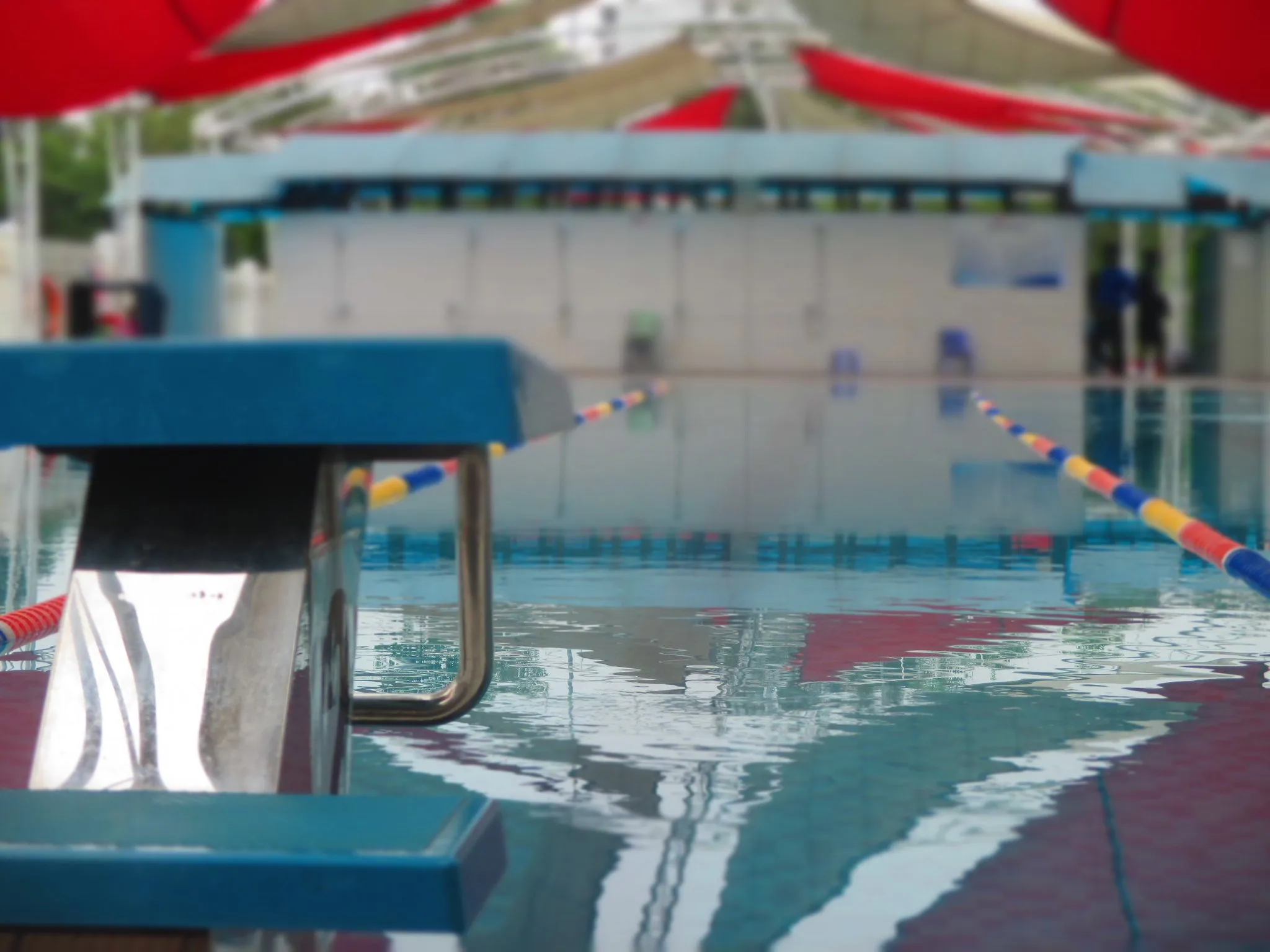 A bright turquoise outdoor swimming pool in full sun, seen across the water