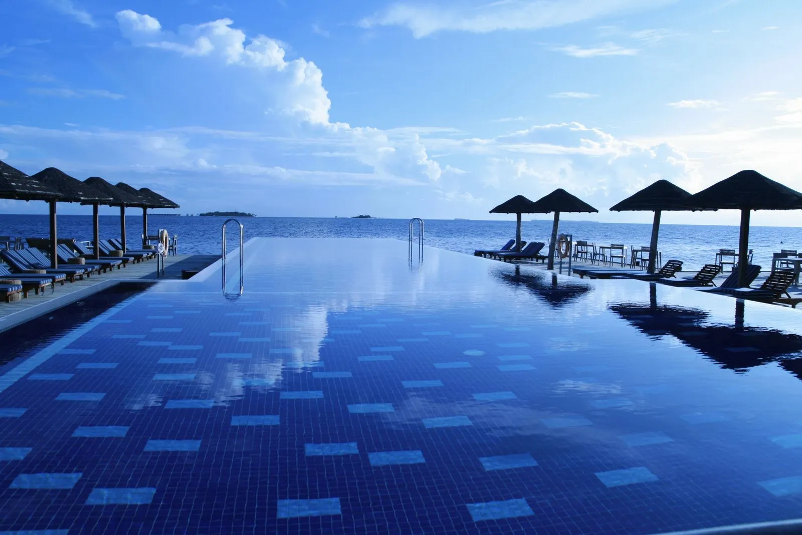 Lounge chairs lined along the edge of a bright blue swimming pool