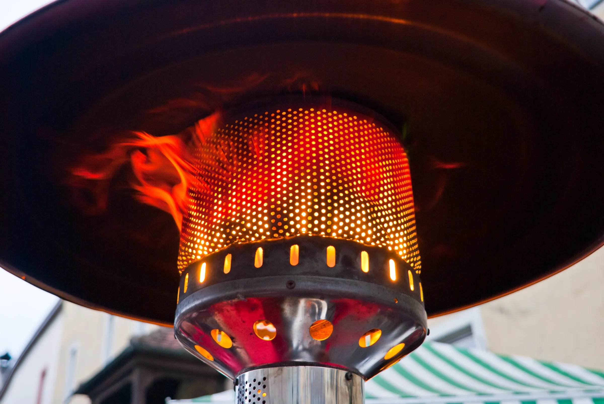 A gas patio heater's perforated burner glowing orange under its reflector dome at dusk, the reason a patio stays in use past September