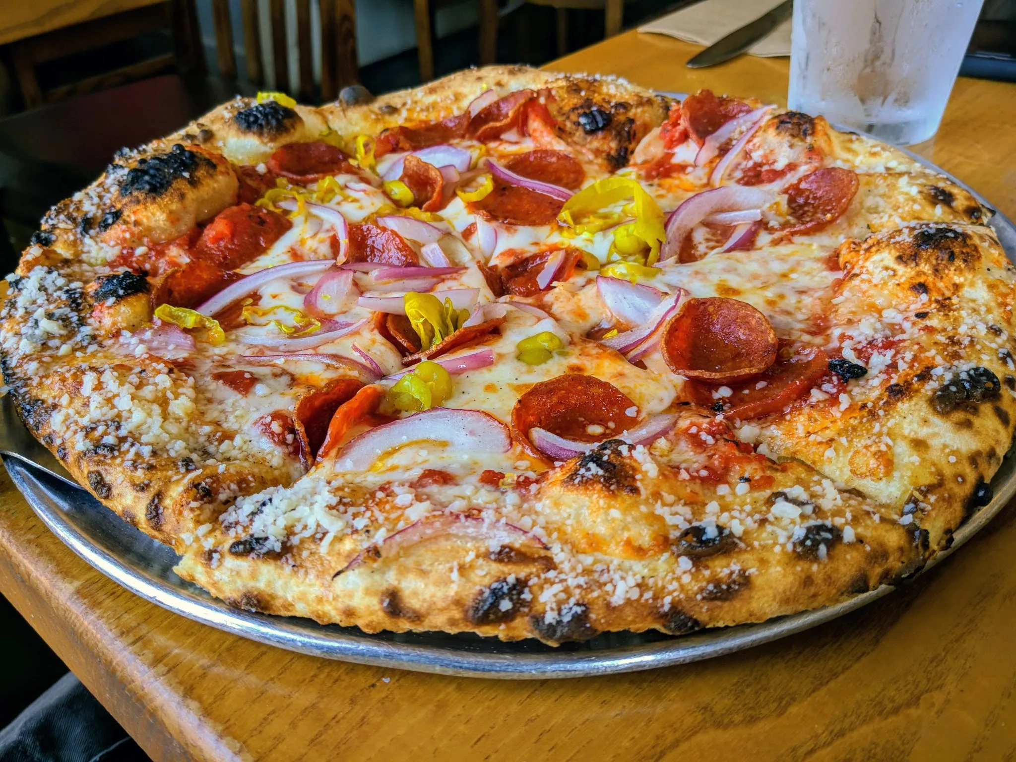 A pepperoni pizza with red onion on a metal tray on a wooden table