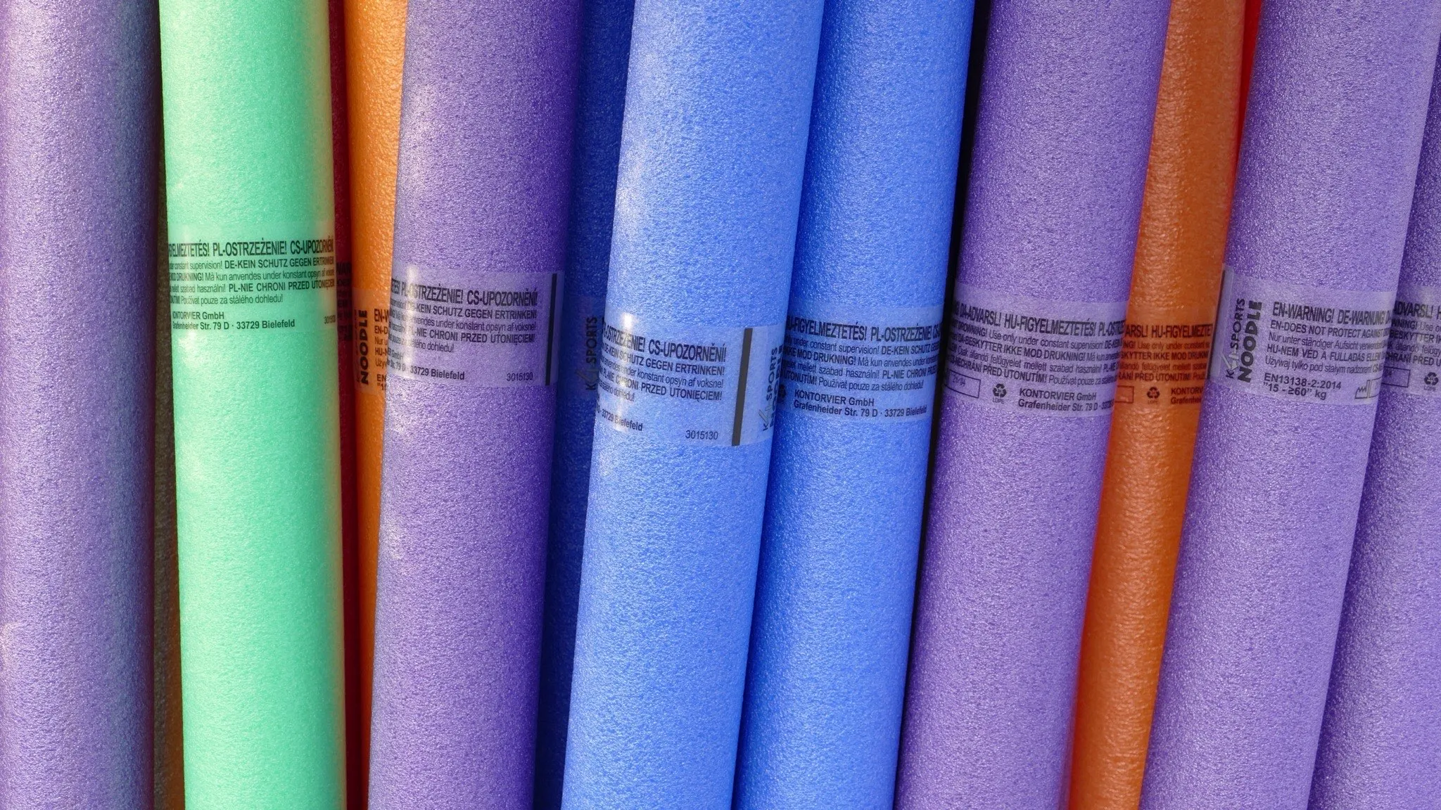 Bins of brightly coloured foam pool noodles standing on end for sale
