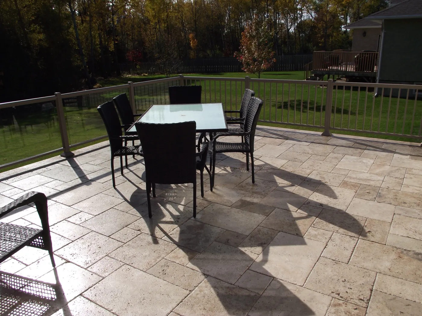 A tumbled travertine paver deck laid in a French pattern, light cream stone with a table and chairs